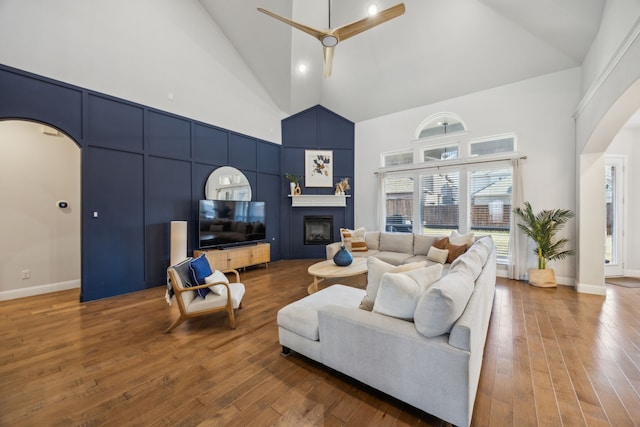 living room featuring hardwood / wood-style floors, a fireplace, arched walkways, and high vaulted ceiling