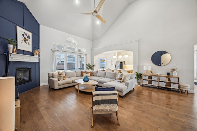 living room with ceiling fan, hardwood / wood-style flooring, arched walkways, a glass covered fireplace, and high vaulted ceiling