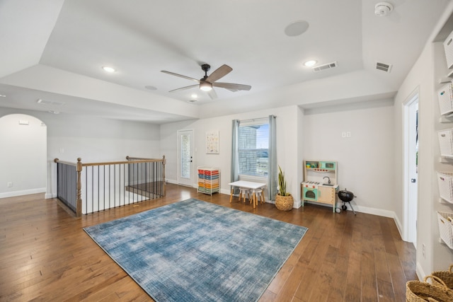 living area with a tray ceiling, visible vents, arched walkways, and hardwood / wood-style floors