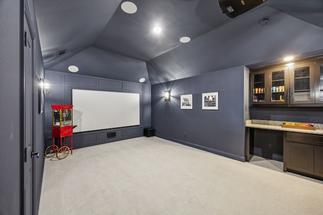 carpeted cinema with visible vents, lofted ceiling, and built in desk