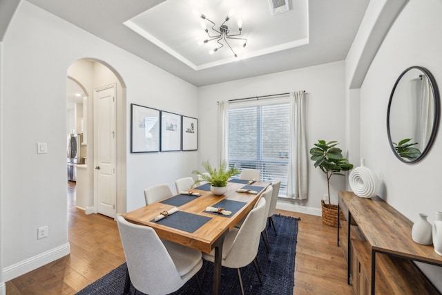 dining space with a tray ceiling, light wood-style flooring, baseboards, and arched walkways