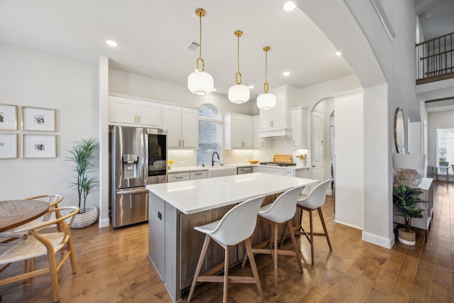 kitchen featuring a sink, backsplash, appliances with stainless steel finishes, arched walkways, and wood-type flooring