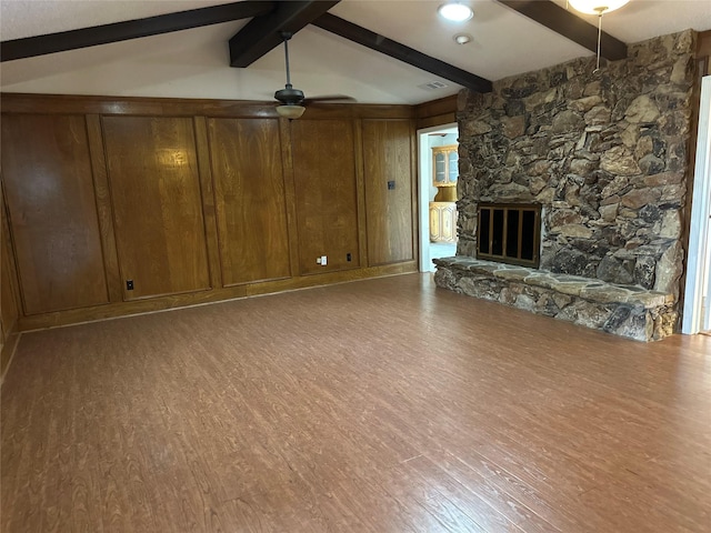 unfurnished living room featuring ceiling fan, a stone fireplace, wood finished floors, and lofted ceiling with beams