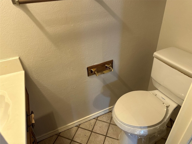 bathroom with toilet, baseboards, and a textured wall