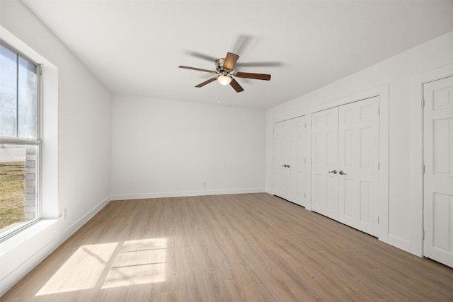 unfurnished bedroom featuring two closets, light wood-type flooring, baseboards, and a ceiling fan