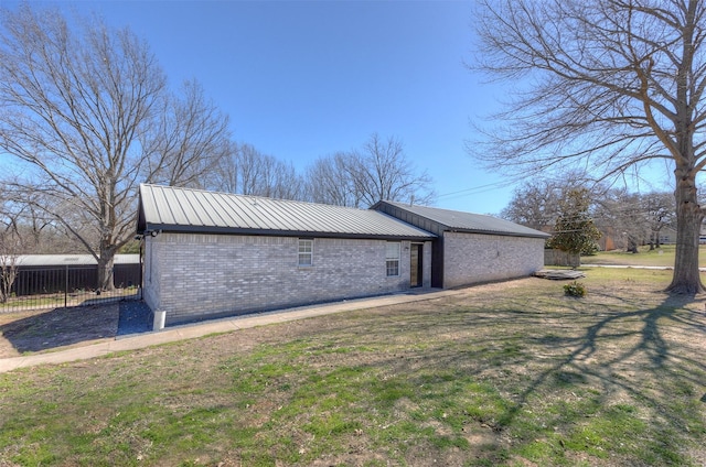 view of side of home featuring brick siding, a lawn, metal roof, and fence