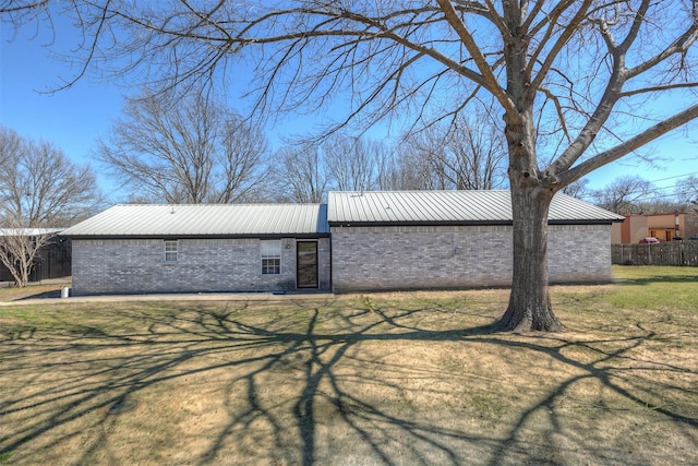 view of property exterior with a yard, fence, brick siding, and metal roof