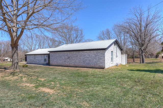 view of home's exterior featuring a lawn, brick siding, and metal roof