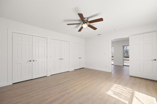 unfurnished bedroom with a ceiling fan, baseboards, multiple closets, and light wood-type flooring