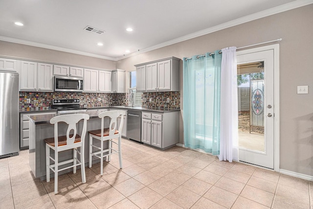 kitchen featuring visible vents, ornamental molding, a center island, stainless steel appliances, and decorative backsplash