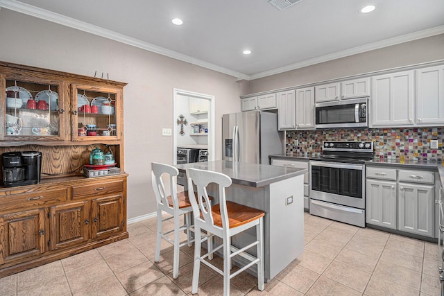 kitchen featuring light tile patterned flooring, ornamental molding, appliances with stainless steel finishes, and washing machine and clothes dryer