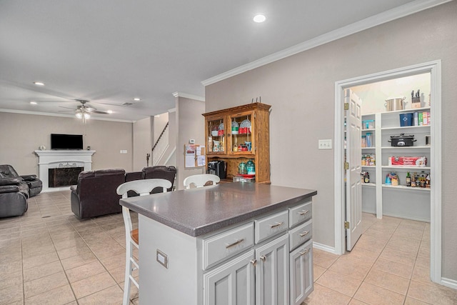 kitchen featuring dark countertops, a breakfast bar area, a fireplace, crown molding, and light tile patterned floors