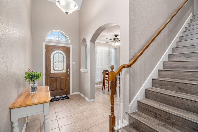 foyer entrance featuring light tile patterned floors, baseboards, arched walkways, and stairs