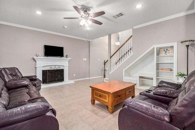 living room with visible vents, a fireplace with raised hearth, stairway, crown molding, and ceiling fan