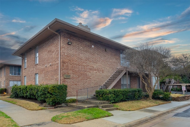 property exterior at dusk featuring brick siding, stairway, and a chimney