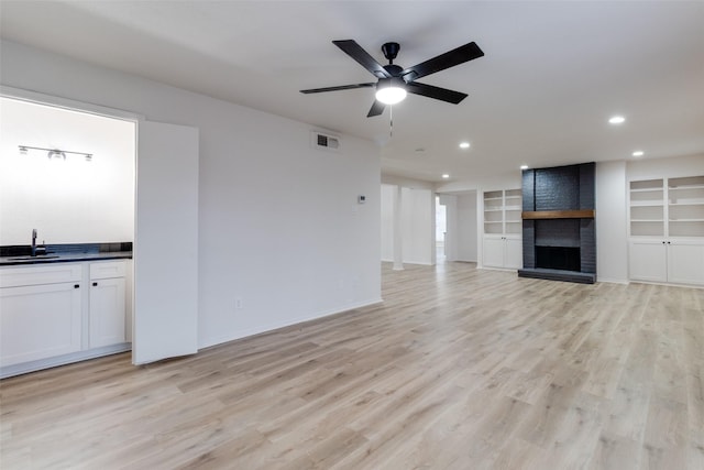 unfurnished living room with a ceiling fan, visible vents, light wood finished floors, a sink, and a brick fireplace