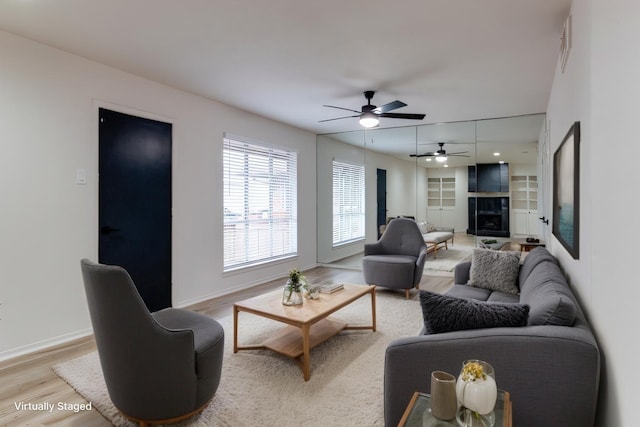 living area featuring built in shelves, baseboards, light wood finished floors, a fireplace, and ceiling fan