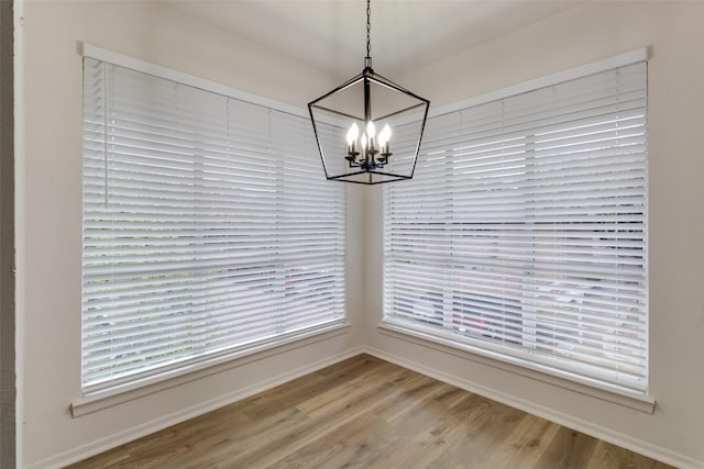 unfurnished dining area with an inviting chandelier, wood finished floors, and baseboards