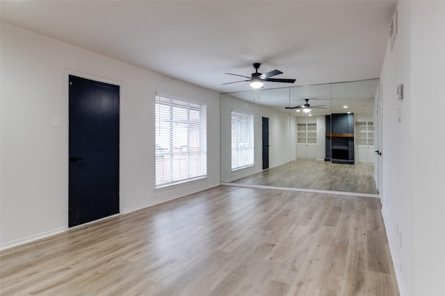 unfurnished living room with a large fireplace, ceiling fan, baseboards, built in features, and light wood-style floors