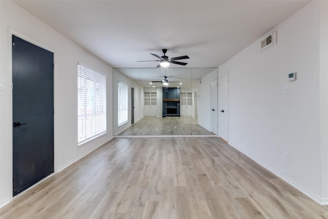 unfurnished living room featuring light wood-type flooring, built in shelves, a ceiling fan, a fireplace, and baseboards