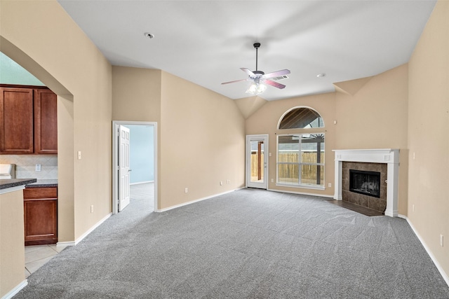 unfurnished living room featuring baseboards, vaulted ceiling, light carpet, a fireplace, and a ceiling fan