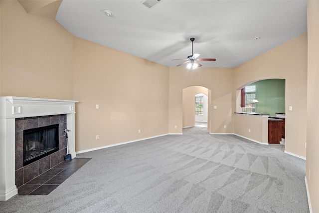 unfurnished living room featuring baseboards, ceiling fan, carpet flooring, a fireplace, and arched walkways