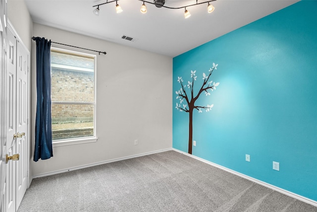 carpeted spare room featuring visible vents, baseboards, and rail lighting