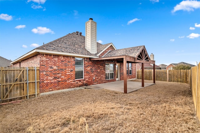 back of property with a patio, a yard, a fenced backyard, a chimney, and brick siding