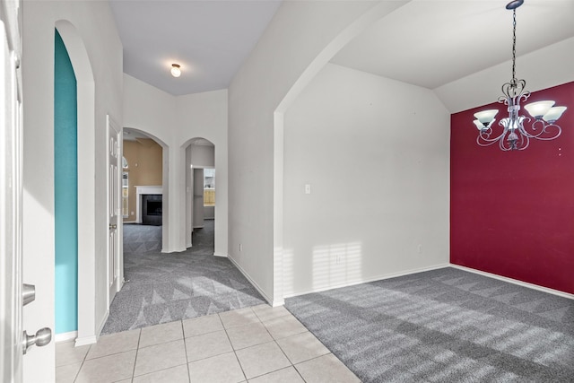 foyer entrance featuring light tile patterned floors, baseboards, light colored carpet, a chandelier, and a tile fireplace