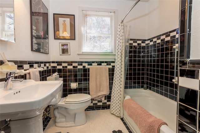 bathroom with tile patterned floors, a wainscoted wall, shower / bath combo with shower curtain, toilet, and tile walls