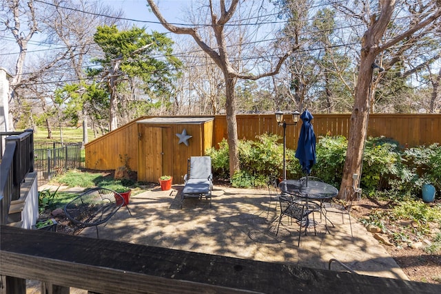 view of patio featuring an outbuilding, a storage unit, a fenced backyard, and outdoor dining area