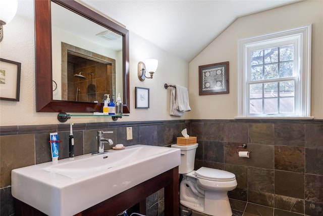 full bathroom featuring toilet, tile walls, wainscoting, vanity, and vaulted ceiling