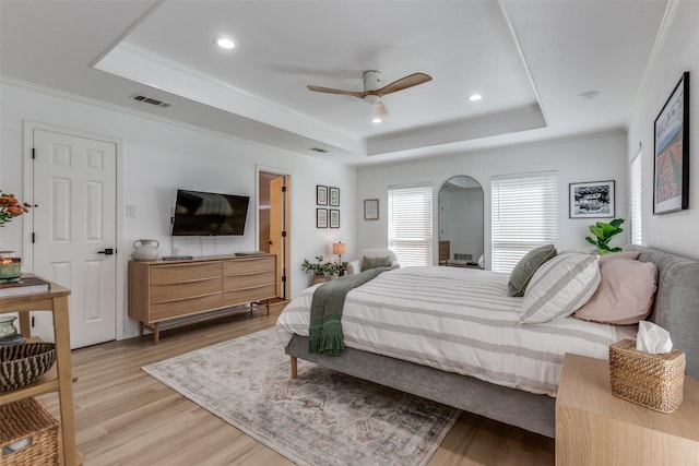 bedroom with a tray ceiling, visible vents, crown molding, and light wood finished floors