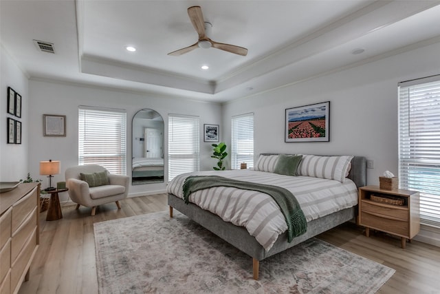 bedroom featuring a raised ceiling, recessed lighting, crown molding, and light wood finished floors