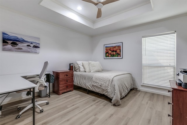 bedroom featuring light wood finished floors, crown molding, ceiling fan, baseboards, and a tray ceiling