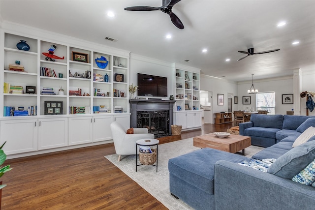 living room featuring visible vents, a fireplace, dark wood-type flooring, crown molding, and ceiling fan with notable chandelier