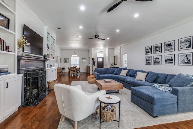 living room with crown molding, dark wood-style flooring, and ceiling fan with notable chandelier