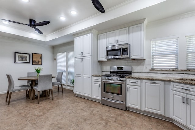 kitchen featuring backsplash, a tray ceiling, ornamental molding, stainless steel appliances, and a ceiling fan