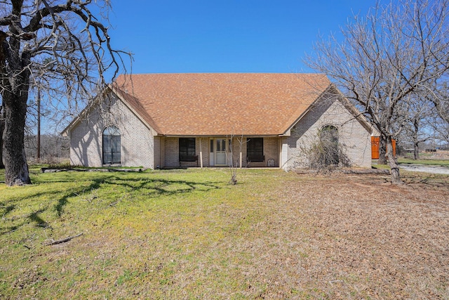 view of front facade featuring a front yard, brick siding, and roof with shingles