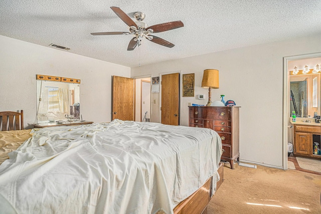 bedroom featuring visible vents, connected bathroom, light carpet, a textured ceiling, and a ceiling fan