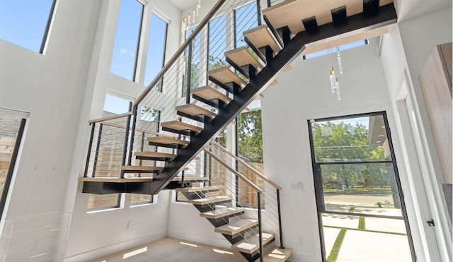 stairs featuring baseboards, wood finished floors, and a towering ceiling