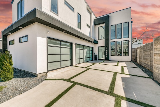 garage at dusk with concrete driveway and fence