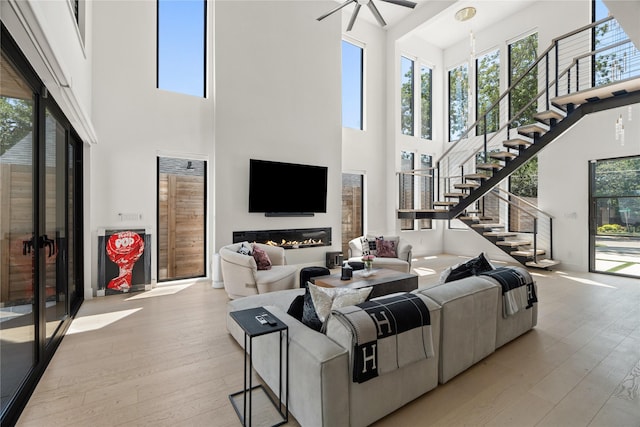 living room featuring stairway, light wood-style flooring, a ceiling fan, and a glass covered fireplace