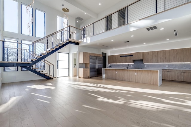 unfurnished living room with visible vents, recessed lighting, a sink, stairs, and light wood-type flooring