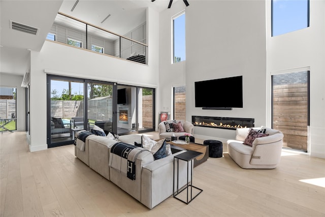 living room with visible vents, baseboards, a glass covered fireplace, and light wood finished floors