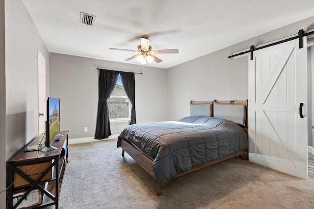 carpeted bedroom featuring a ceiling fan, a barn door, baseboards, and visible vents