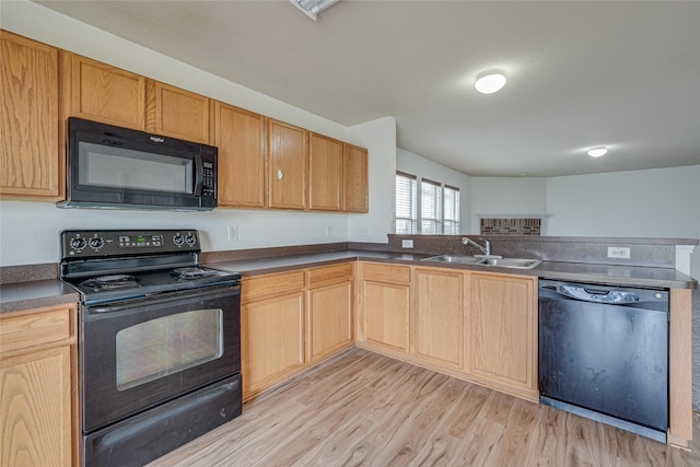 kitchen with black appliances, dark countertops, light wood finished floors, and a sink