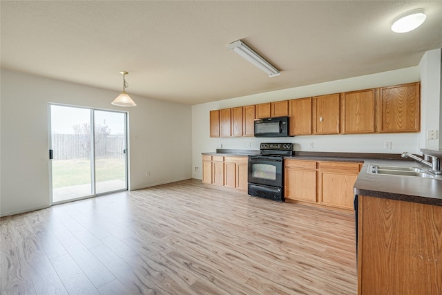 kitchen featuring a sink, light wood-style floors, dark countertops, and black appliances