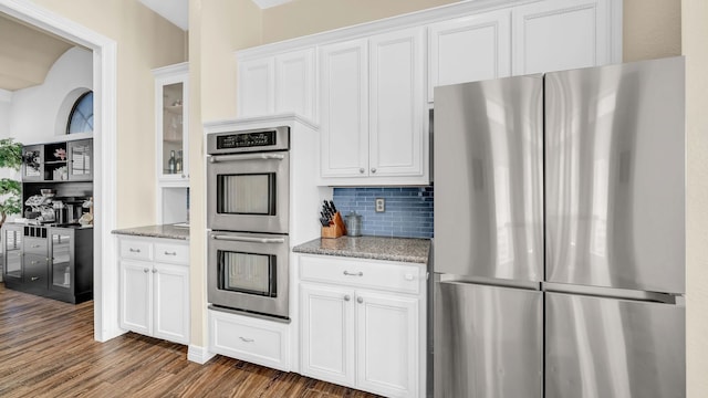 kitchen featuring stainless steel appliances, light stone countertops, dark wood-style floors, and white cabinets