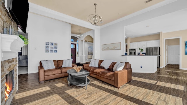 living room with baseboards, a stone fireplace, arched walkways, a notable chandelier, and dark wood-style flooring